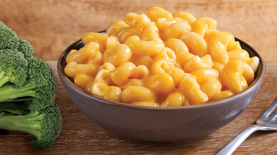 Un plato de macarrones con queso de Stouffer sobre una mesa con un tenedor y manojos de brócoli.