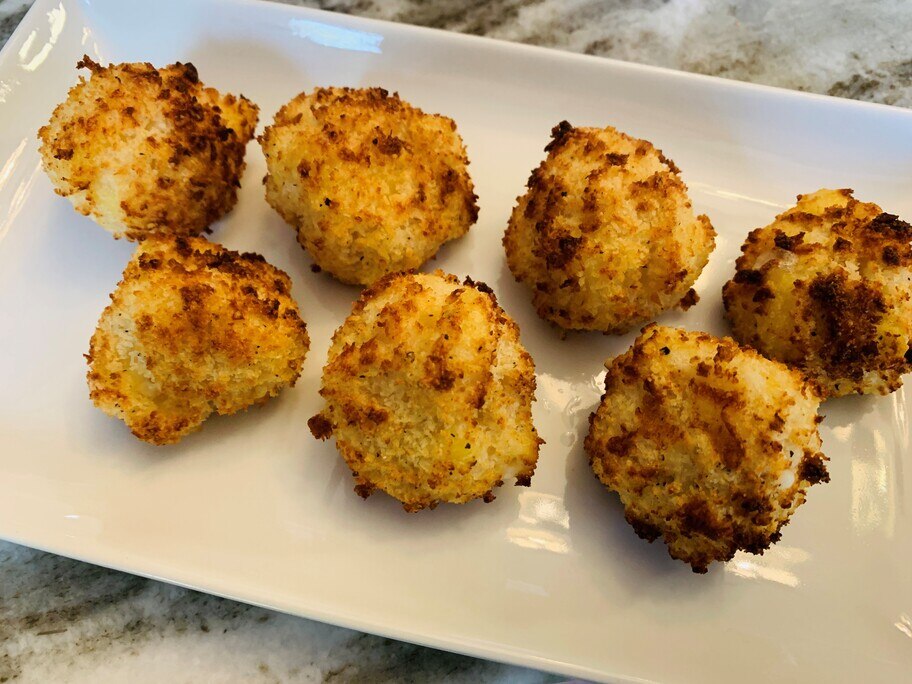 Siete bocaditos de macarrones con queso en un plato blanco sobre una mesa de cocina.