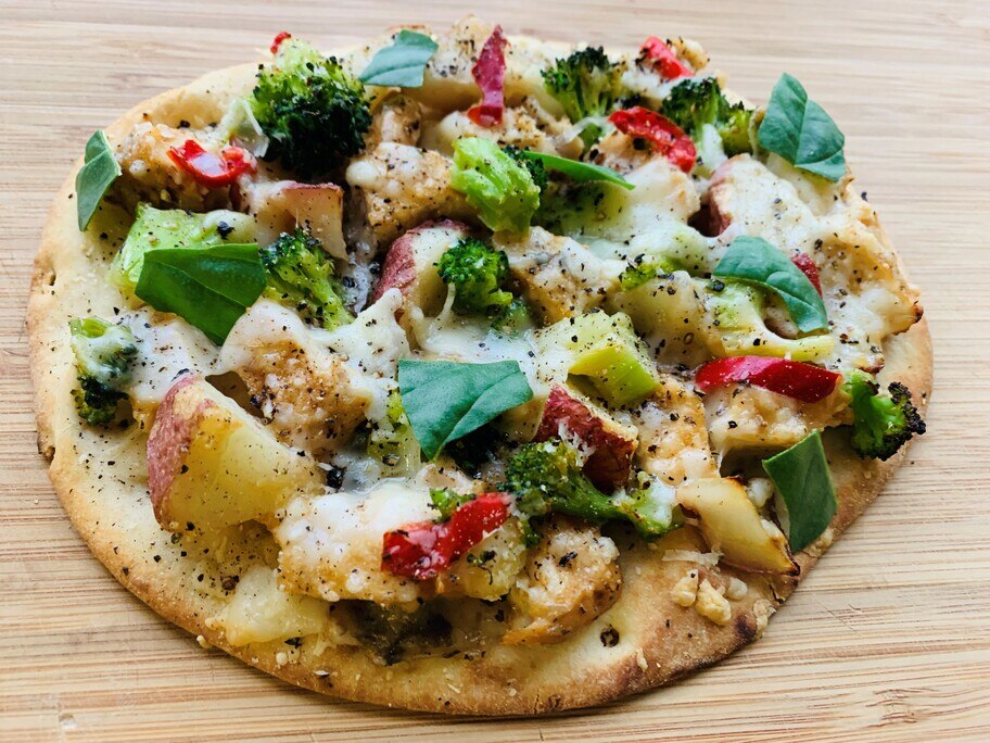 Un pan plano de pollo asado a las hierbas, con brócoli y albahaca, sobre una mesa de madera.
