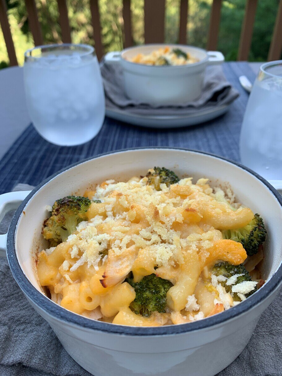 Una mesa de patio tendida con vasos de agua, servilletas y dos cazuelas con macarrones con queso al horno con brócoli.