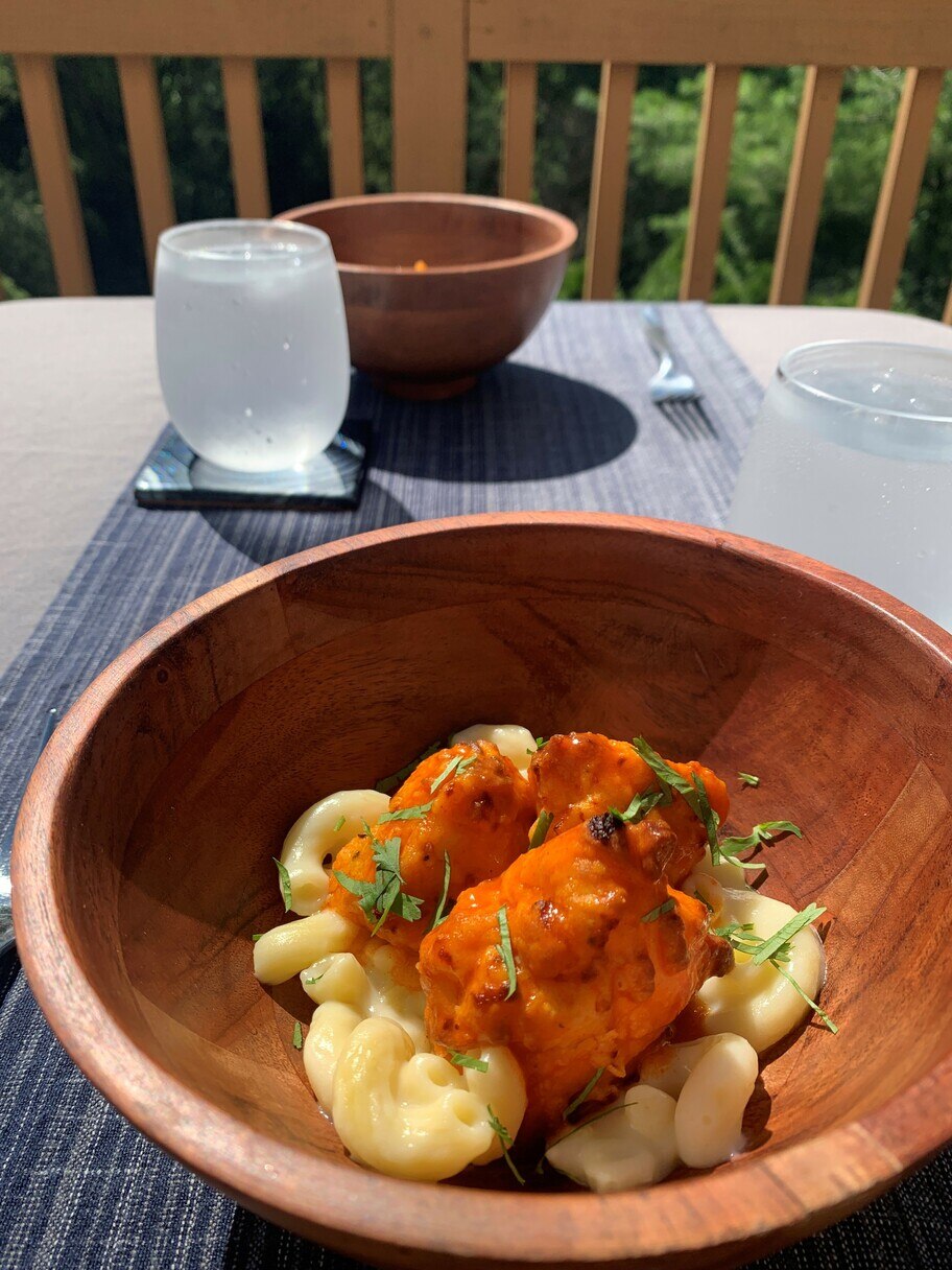 Mesa de patio con vasos de agua, mantel, servilletas y dos tazones de madera con macarrones con queso y pollo estilo Buffalo.
