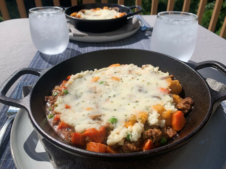 Una mesa de patio tendida con vasos de agua, un mantel, servilletas y dos platos de hierro llenos de pastel del pastor.