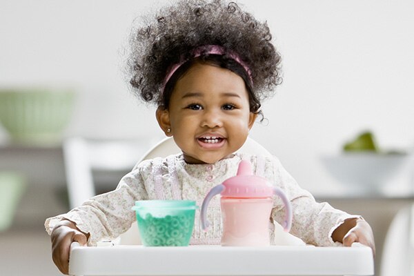 Photograph of a 1 year-old girl smiling in a pink headband, white long sleeve shirt, and pink pants.