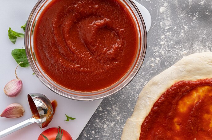 Una tabla de madera con tomates, ajo y albahaca repartidos sobre una superficie de madera con un tazón de salsa y más ajo.