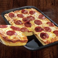 Una pizza de masa horneada en molde, crujiente, de pepperoni, cortada en rebanadas cuadradas en un molde