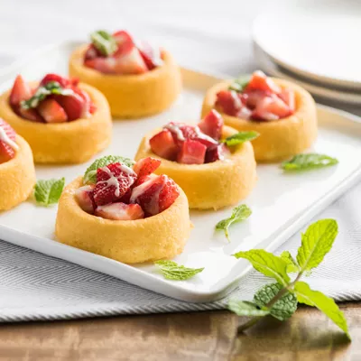 Six strawberry dessert cups lined up on a white plate with mint garnish.